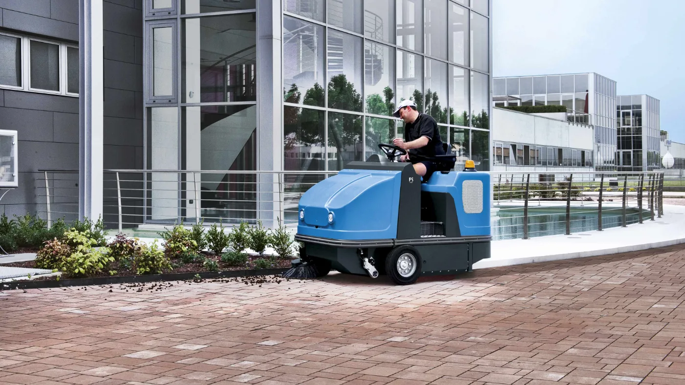 Ride-on sweeper clearing loose debris from a commercial floor
